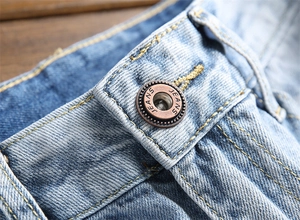 Gros plan sur le bouton en bronze vintage et les coutures de ce jean délavé bleu clair