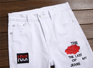 Detail of white denim jeans with red rose embroidery and black letter patches