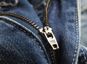 Makro-Detail des bronzenen SBS-Metallreißverschlusses und der dunkelblauen Denim-Nähte