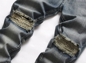 Detailaufnahme einer blauen Jeans mit großen Rissen am Knie und weißen Fransen-Details