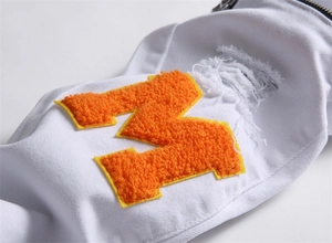 Detail of orange chenille M patch and distressed denim on white streetwear jeans