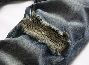 Makro-Detail der handgefertigten Risse am Knie mit Fransen an blauen Jeans im Washed-Look