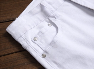 Detail of white cotton denim pocket with silver rivets on dark wood background