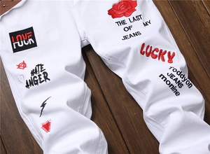 Detail of white cotton jeans featuring red rose embroidery and street style graphic prints