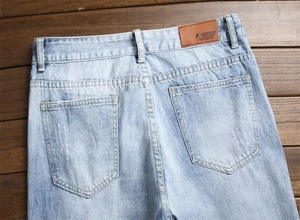 Détail de l'arrière d'un jean bleu clair avec écusson en cuir et poches arrière