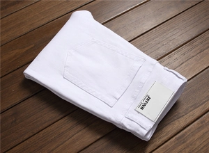 Detailed close-up of white denim jeans with a classic leather brand patch on wood background
