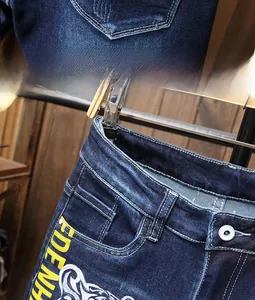 Detail of heavy embroidery and yellow letter print on dark blue straight-leg jeans