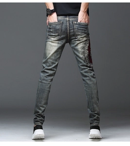 Détail d'un jean délavé vintage avec une grande broderie de plumes rouges et noires