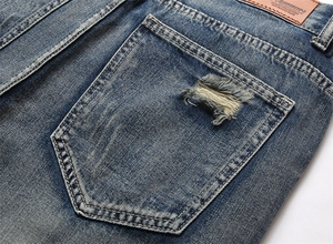 Detailansicht der Gesäßtasche aus blauem Denim mit Used-Look und braunem Lederpatch