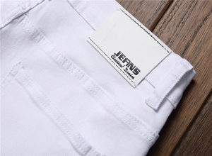 Detail shot of white denim jeans featuring a leather brand patch with classic stitching