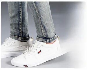 Detail shot of slim-fit men's distressed jeans paired with white crocodile pattern sneakers