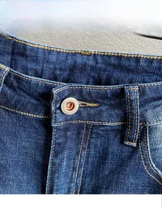 Detailansicht einer Jeans mit handgefertigtem Metallknopf und gelben Kontrastnähten