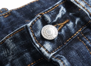 Gros plan du bouton métallique gravé sur un jean denim bleu délavé avec surpiqûres jaunes