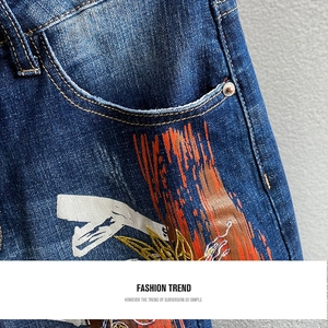 Detail der blauen Jeans mit künstlerischem orangefarbenem Sprühdruck und Metallnieten