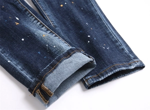 Gros plan d'un ourlet de jean bleu foncé avec éclaboussures de peinture et coutures