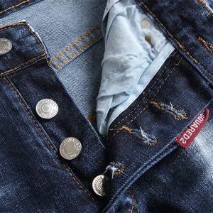 Gros plan d'un jean punk bleu ajusté montrant la braguette boutonnée et l'étiquette rouge