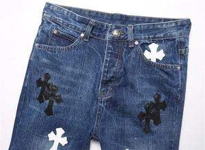 Dettaglio dei jeans blu con toppe a croce in pelle e bottone argentato inciso a mano