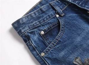 Dettaglio dei jeans blu denim con toppa in pelle a croce e borchie metalliche logate