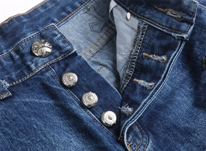 Macro dei bottoni in metallo argentato con croce su jeans in denim blu pesanti