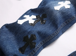 Dettaglio del ricamo a croce stile punk su jeans slim fit in denim blu scuro di qualità