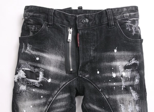 Detail of ripped black wash jeans featuring paint splatters and red tag branding