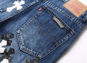 Dettaglio di jeans blu con toppe a croce in pelle e targhetta metallica con logo
