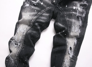 Detail of distressed black denim jeans with white paint splatters and ripped effects