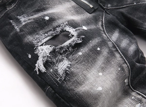 Detail of black washed denim jeans featuring distressed holes and white paint splatters