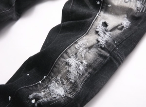 Detail of distressed grey jeans featuring white paint splatters and ripped frayed edges