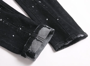 Detail view of black ripped jeans featuring white paint splatters and rolled-up cuffs