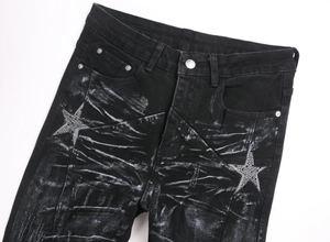 Detailed shot of black flared jeans with distressed star patchwork and metallic studs
