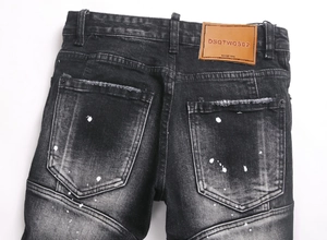 Detail of the brown leather waist patch on distressed black denim jeans with paint splatters