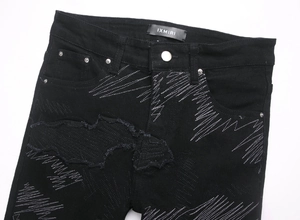 Gros plan d'un jean noir avec broderies blanches en zigzag et détails usés et déchirés