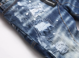 Detail of blue distressed denim jeans with paint splatters and black zipper accents