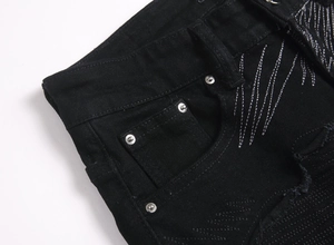 Détail macro du jean slim noir avec broderie argentée et poche à rivets métalliques