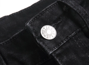 Macro shot of silver metal button with JEANS engraving on black stretch denim pants