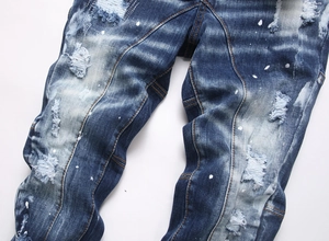 Close-up of distressed blue denim featuring heavy wash, ripped holes and white paint splatters