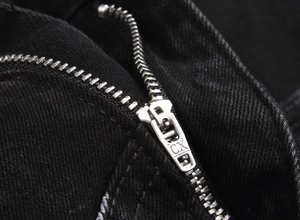Macro shot of silver metal zipper with CX engraving on black slim fit denim fabric