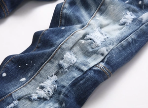 Detail of distressed dark blue jeans with ripped holes and white paint splatters