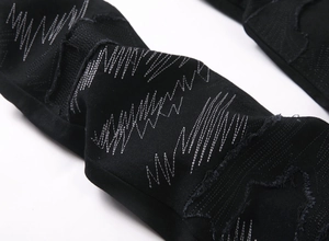 Détail du jean noir avec broderie de vagues argentées et textures de déchirures usées