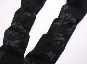 Détails de broderies blanches en zigzag et déchirures sur un jean noir évasé de style punk