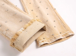 Detail der gelben, schmal geschnittenen Schlagjeans mit silbernem Straßbesatz auf Denim