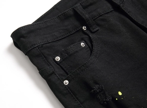 Detail of black distressed denim with yellow paint splatter and silver rivet accents