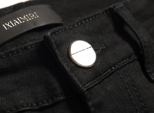 Detail of black stretch denim waist featuring silver metal button and leather brand tag