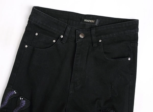 Detail der lila Schlangen-Paillettenstickerei und Rissstruktur auf schwarzer Jeans