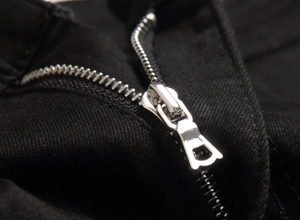 Macro shot of silver metal zipper detail on black stretch embroidered denim jeans