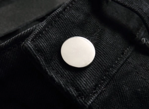Nahaufnahme eines silbernen Metallknopfs an einer schwarzen Jeans mit präzisen Nähten