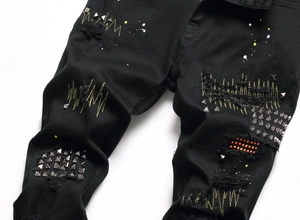 Detail of black denim jeans with metal studs, embroidery, and distressed ripped effects