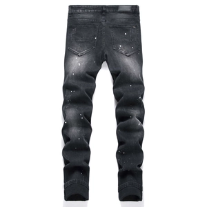 Dettaglio di jeans neri usurati con macchie di vernice bianca e toppa in pelle