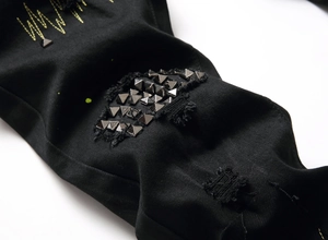 Detail of distressed black denim with pyramid studs, embroidery and frayed edges